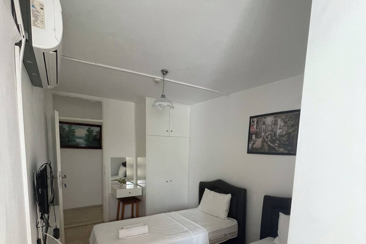 A hotel room with two single beds, a desk with a chair, a small table, and an air conditioning unit.