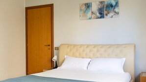 Quarto com uma cama grande, uma porta de madeira e três quadros abstratos na parede.