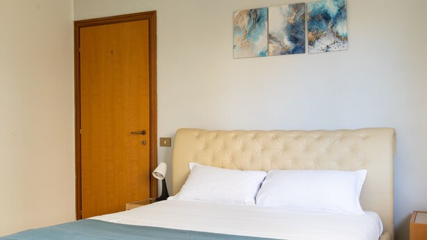A bedroom with a large bed, a wooden door, and three abstract paintings on the wall. - Alessandrino Apartment (Rome)