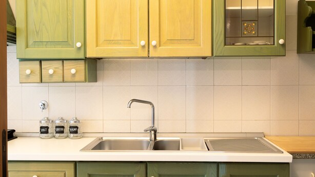 Cozinha com armários verdes, pia de aço inoxidável e painel de azulejos.