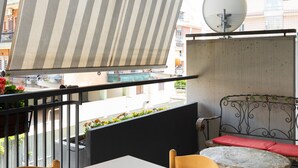 A balcony with a striped awning, a round table, a wicker sofa with a red cushion, and a satellite dish. - Alessandrino Apartment (Rome)