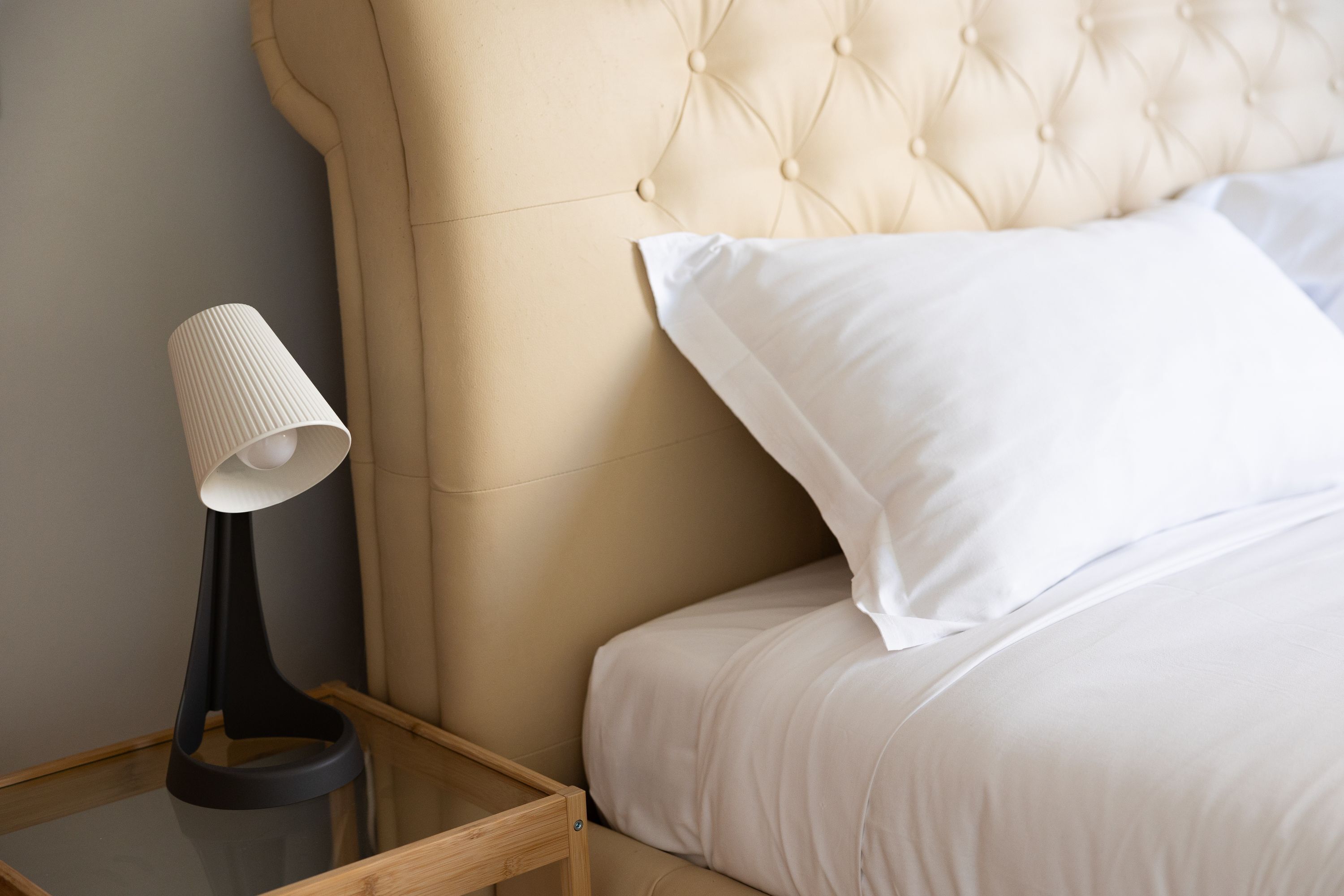 A neatly made bed with a tufted headboard, a bedside lamp, and a wooden nightstand.