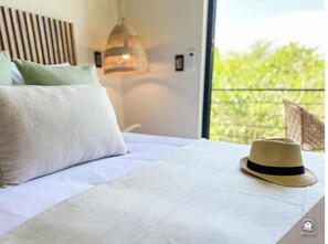 Une chambre d’hôtel avec un lit, des oreillers, un chapeau et un luminaire suspendu.