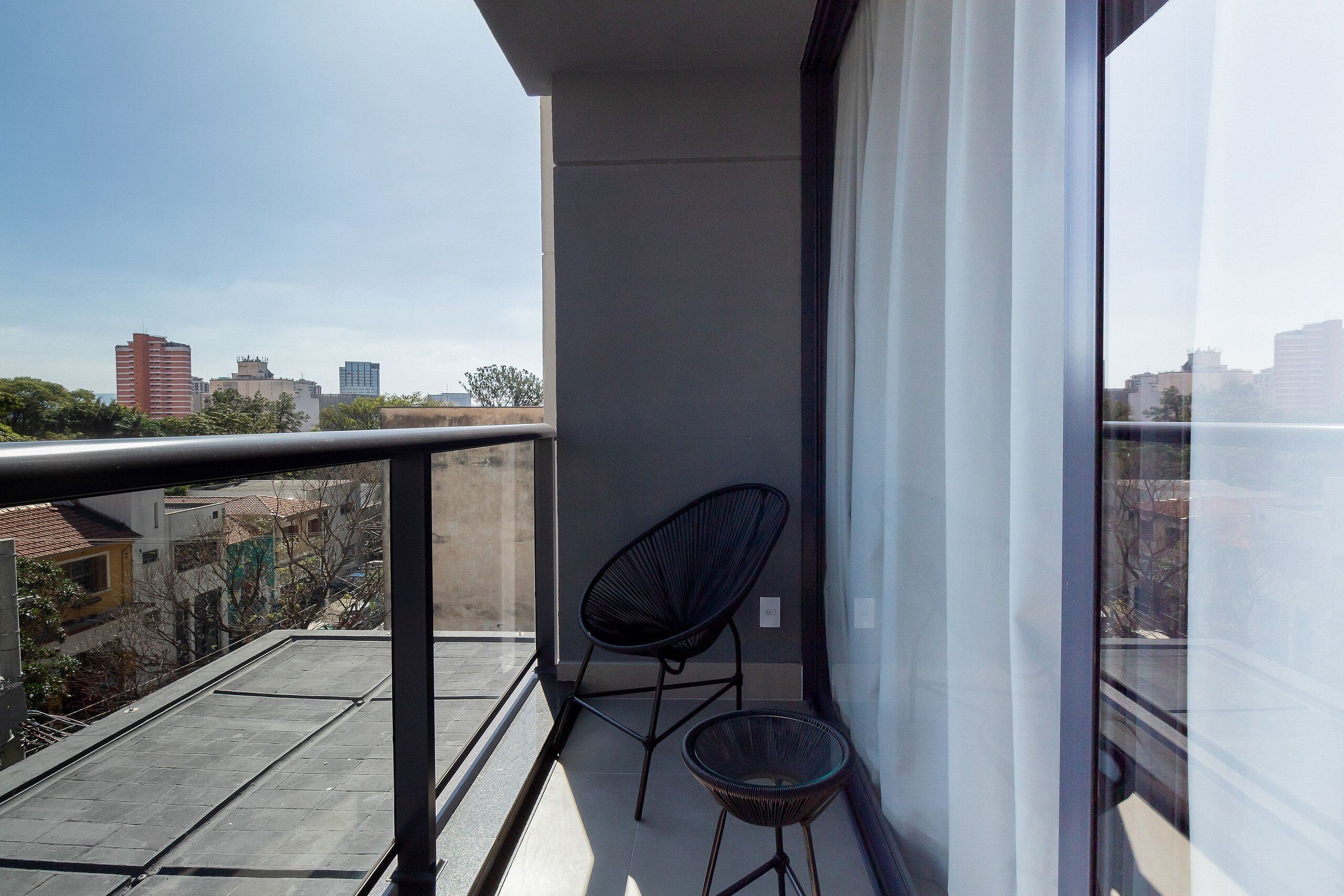 A balcony with a view of the cityscape, a black chair, and a small round table.