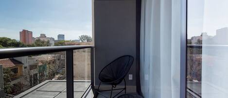 A balcony with a view of the cityscape, a black chair, and a small round table.
