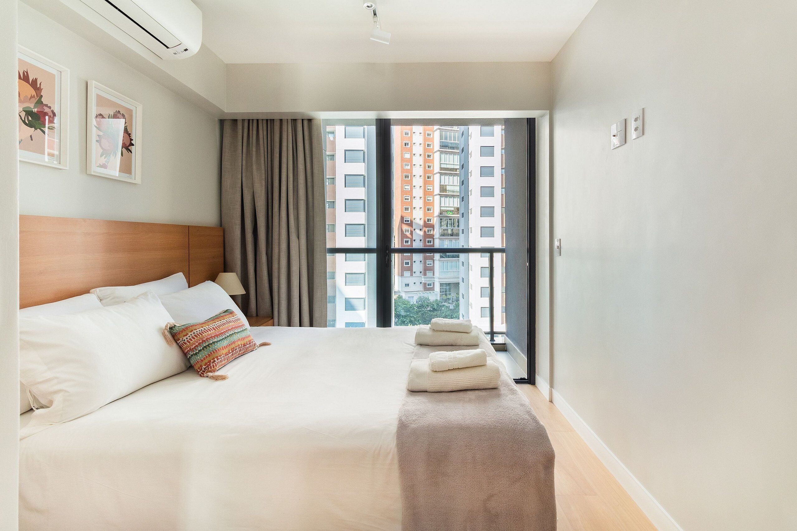 Ein Hotelzimmer mit einem großen Bett, einem Kopfteil, einem Fenster mit Vorhängen und Blick auf Gebäude.