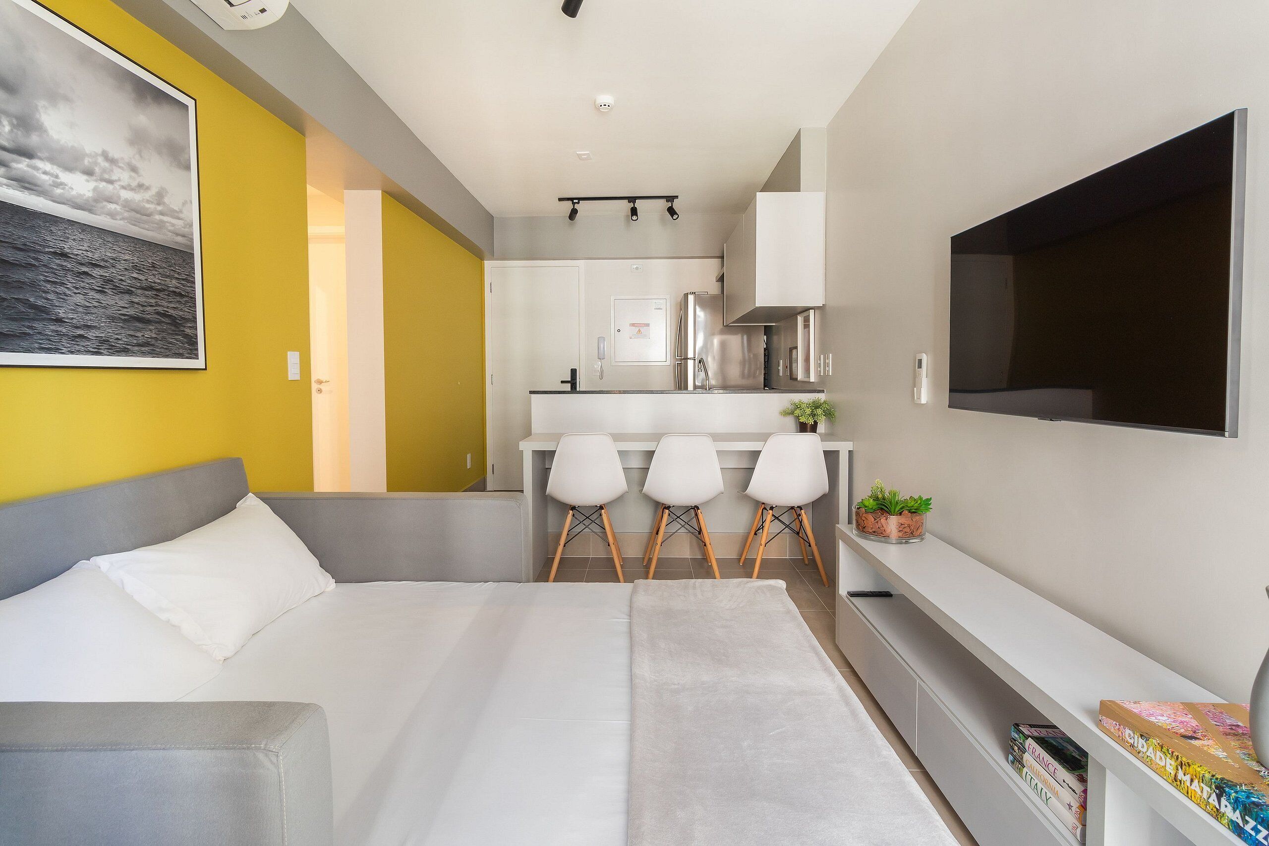 A modern, compact living space with a bed, a small kitchenette, a TV, and a dining area with chairs.
