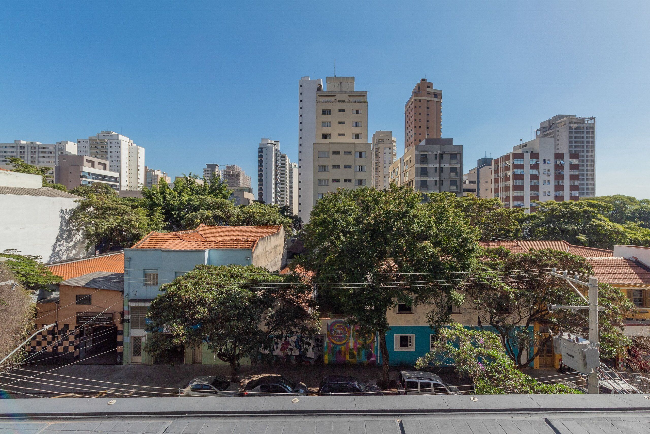 A cityscape with tall buildings, trees, and a colorful mural on a building.