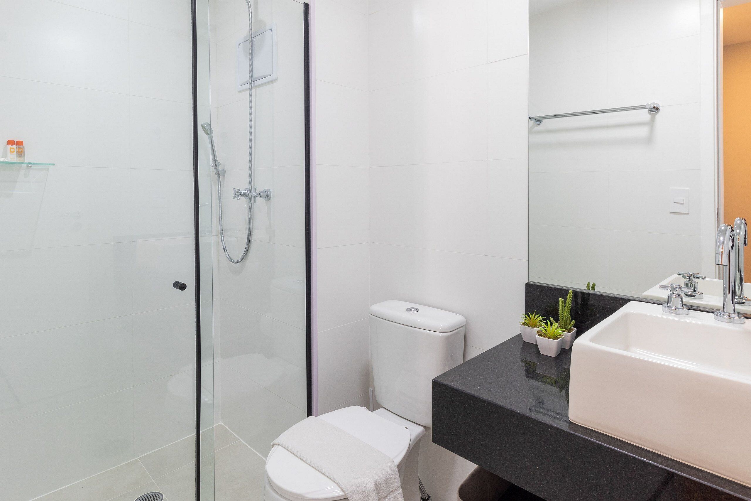 Un baño moderno con cabina de ducha de cristal, inodoro blanco, encimera negra y lavabo blanco con espejo arriba.
