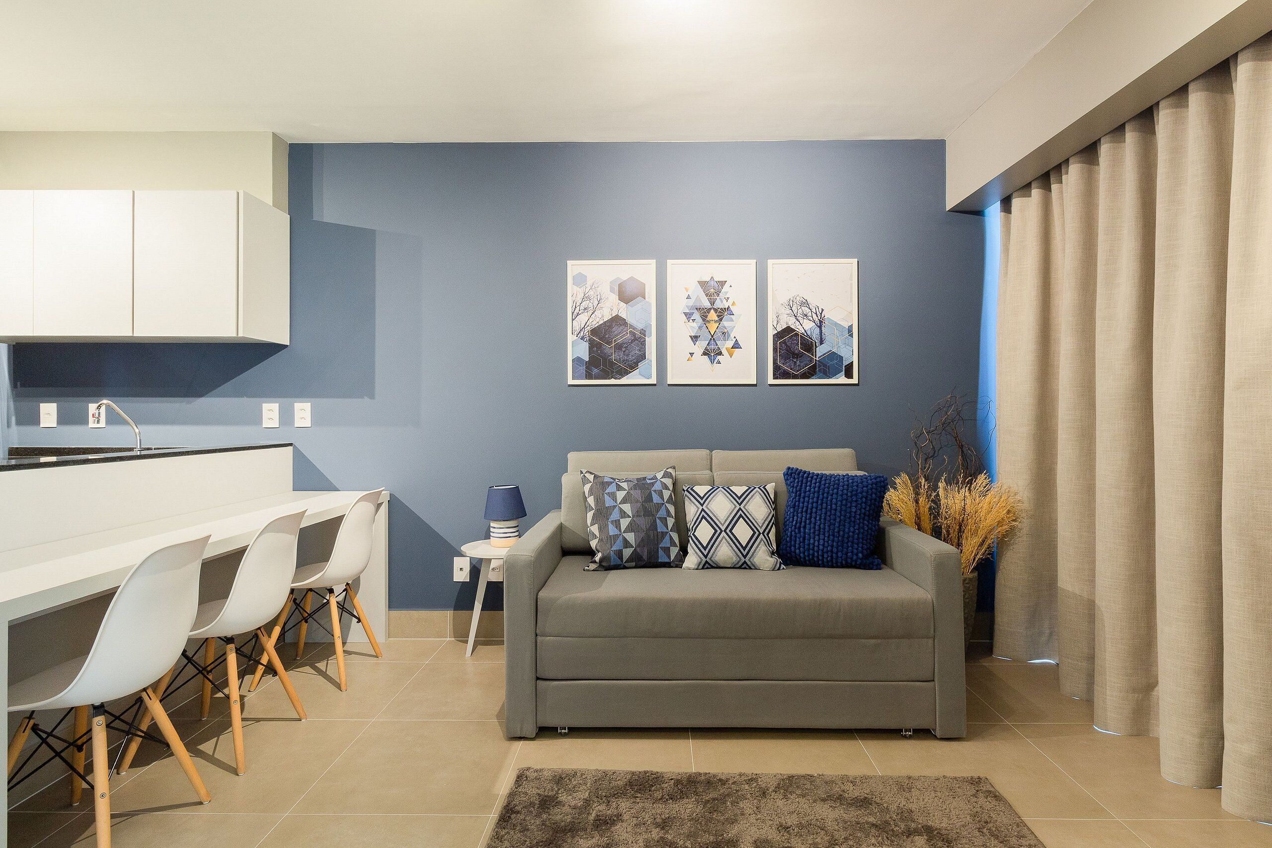 Una sala de estar moderna con un sofá gris, una mesa de comedor con sillas y tres obras de arte colgadas en la pared.