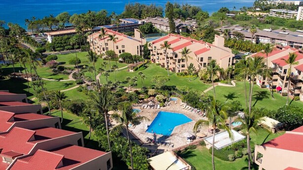 Un resort con varias construcciones, una piscina central y exuberante vegetación.