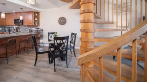 Una cocina moderna con armarios de madera, un comedor con mesa y sillas redondas, y una escalera espiral de madera.
