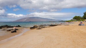 Una playa con cielos despejados, una montaña al fondo y gente disfrutando del agua.