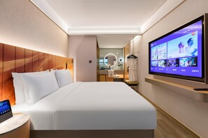 Une chambre d’hôtel moderne avec un grand lit, un téléviseur fixé au mur, une table de chevet et une salle de bain visible à travers une porte ouverte.