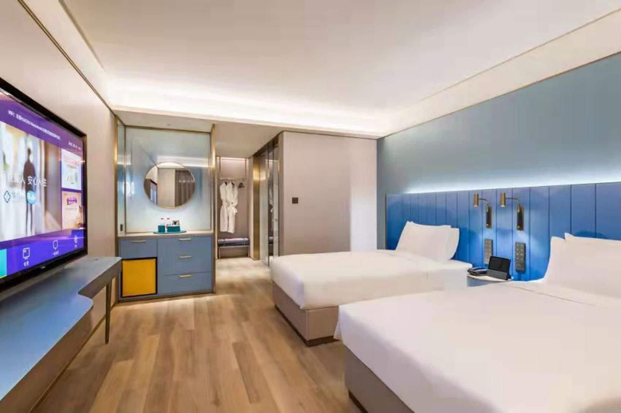 A modern hotel room with two beds, a vanity with a mirror, a television, and a walk-in closet.