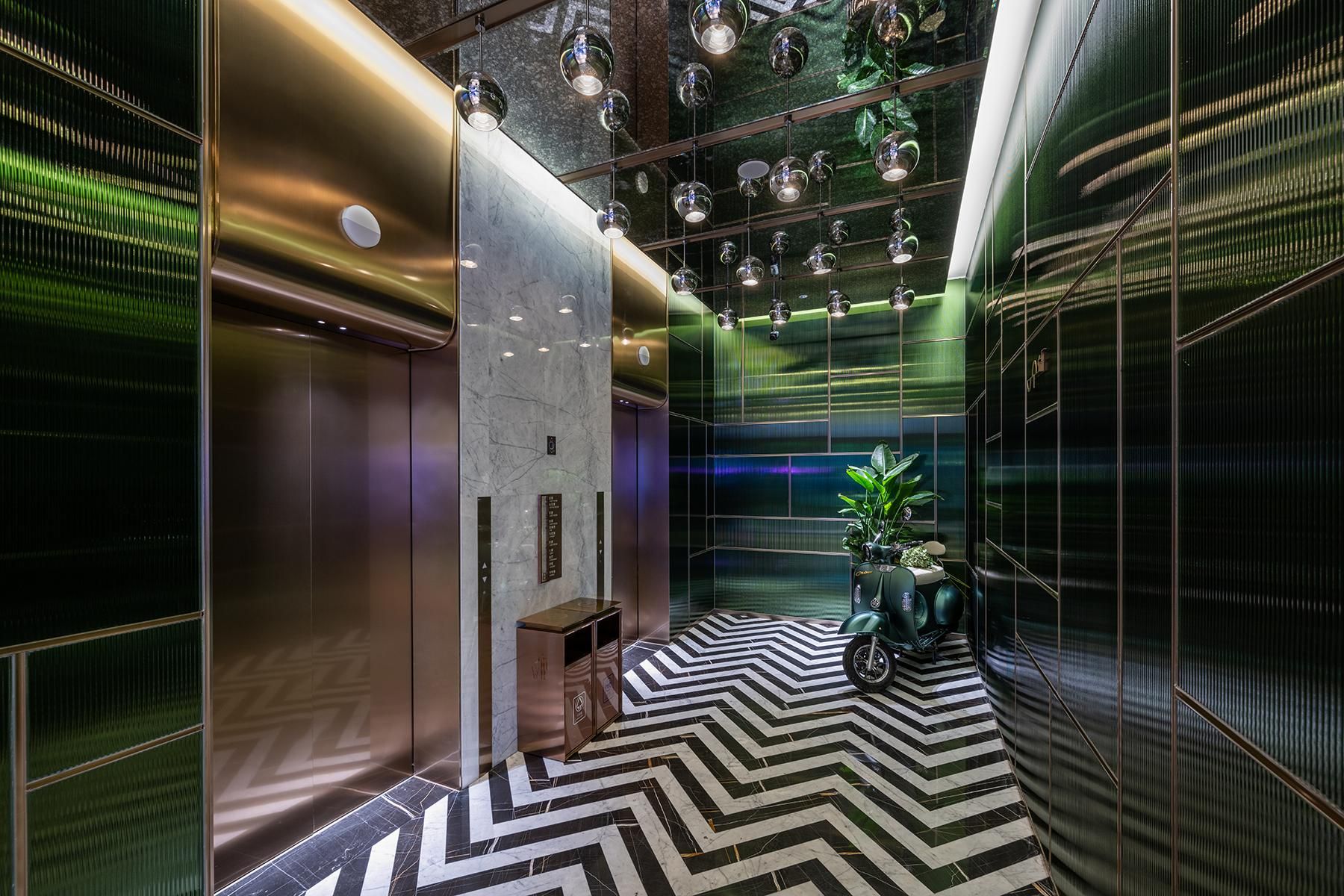 A modern elevator interior with a black and white chevron floor pattern, metallic walls, and hanging spherical lights.
