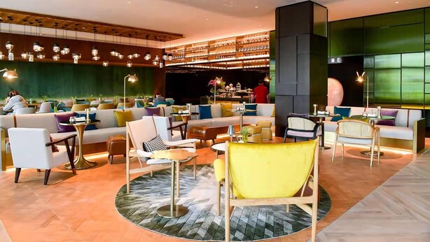 Ein stilvoller Lounge-Bereich mit Sofas, Sesseln und Tischen, inklusive einer Bar und einer großen, grünen Wand.