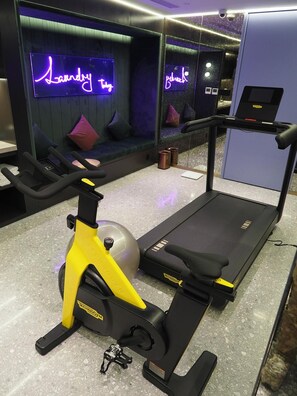 Une salle de sport équipée d'un tapis de course, d'un vélo d'appartement et d'un néon indiquant « Laverie ».