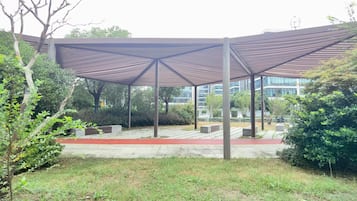 Uma área externa coberta, com design moderno, apresentando estrutura metálica e um caminho vermelho.