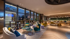 Ein moderner Loungebereich mit Sitzgelegenheiten, Tischen und großen Fenstern mit Blick auf die Stadtlandschaft.