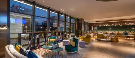 A modern lounge area with seating, tables, and large windows overlooking a cityscape.