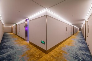 Un pasillo de hotel con piso alfombrado, puertas y una lámpara fijada a la pared.