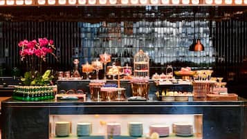 A bar area with a variety of drinks and desserts, a flower arrangement, and a view through the window.