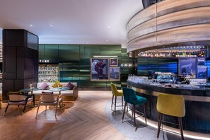 Un espace bar moderne doté d’un comptoir incurvé, de tabourets de bar et d’une étagère bien garnie de bouteilles d’alcool.