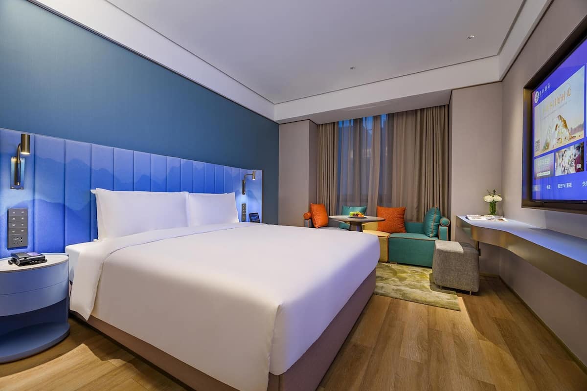 A modern hotel room with a large bed, a seating area with a table, and a TV mounted on the wall.