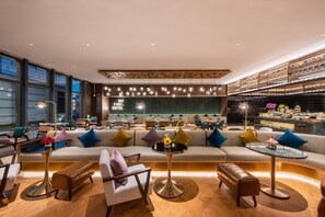 Un espace de détente moderne, doté de canapés, de tables et d’un bar agrémenté d’objets décoratifs.