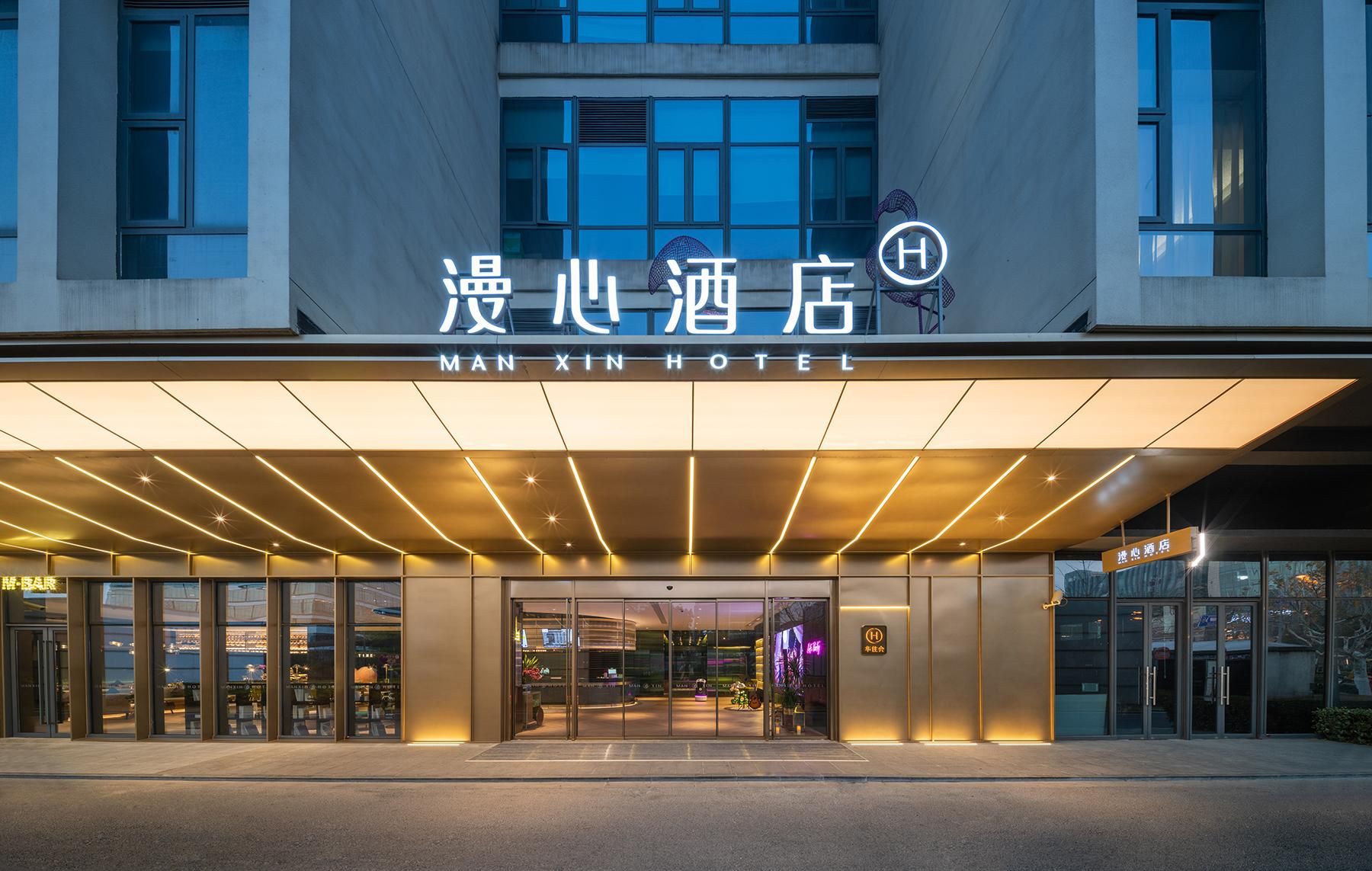The exterior of the Man Xin Hotel with a modern facade, large glass windows, and a prominent entrance.
