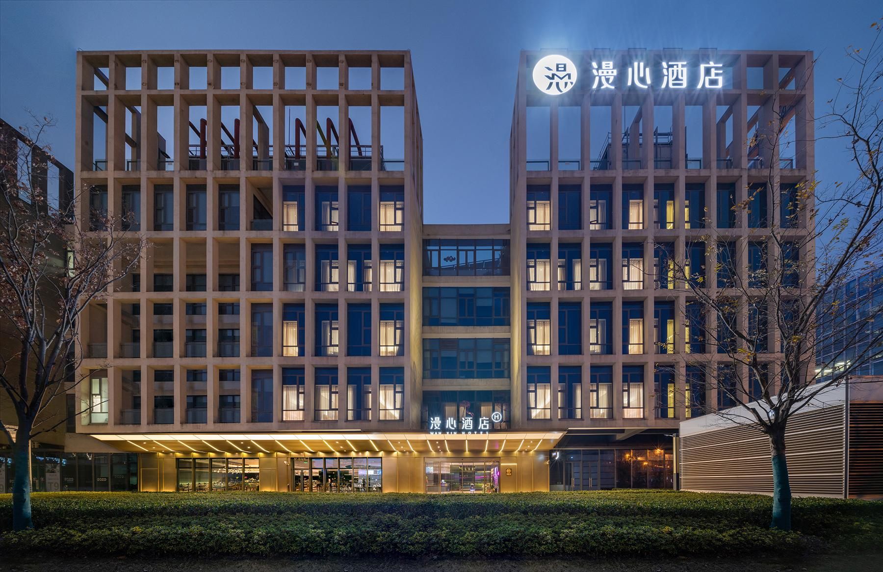 A modern hotel building with a symmetrical facade, multiple floors, and a well-lit entrance.