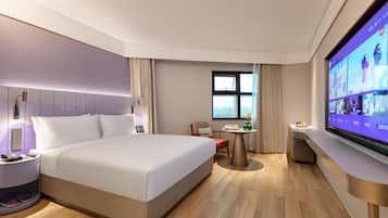 A hotel room with a large bed, bedside tables, a desk with a chair, a television, and a window.