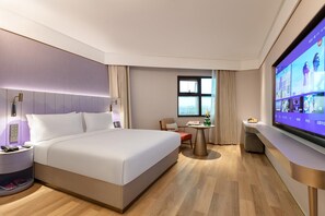 Une chambre d’hôtel avec un grand lit, des tables de chevet, un bureau avec une chaise, une télévision et une fenêtre.