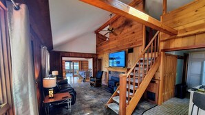 A spacious living area with a wooden interior, a fireplace, a television, and a staircase. - Lakefront cottage on 540 acre Wall Lake / spectacular fishing & sunset views.  (Delton)