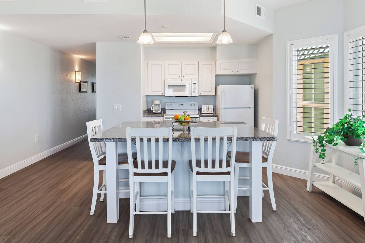 Una cocina moderna con armarios blancos, una isla central con taburetes de bar y un refrigerador.