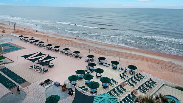 Un patio frente a la playa con mobiliario exterior y vistas al océano.