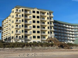 Ein mehrstöckiges Hotel mit Balkonen, einer Holztreppe und Blick auf den Strand.