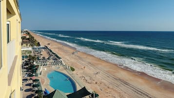 A beachfront hotel with a swimming pool, beach chairs, and umbrellas.