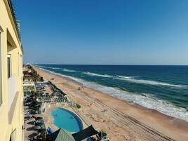 A beachfront hotel with a swimming pool, beach chairs, and umbrellas.