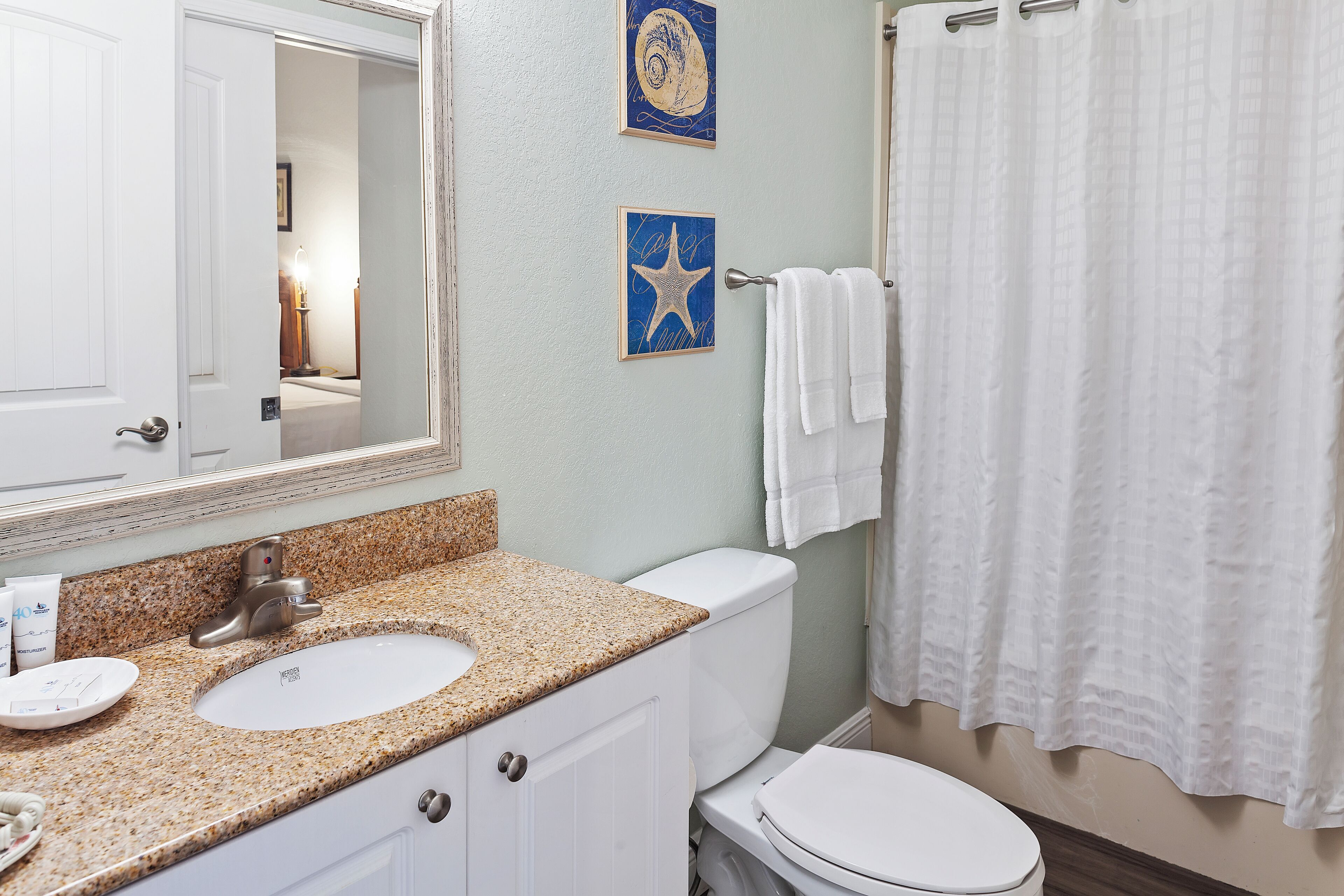 A bathroom with a sink, mirror, toilet, and a shower curtain.