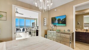 Een slaapkamer met een groot bed, een kroonluchter, een televisie en uitzicht op de oceaan door een schuifdeur.