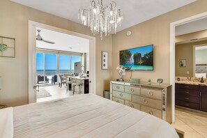 A bedroom with a large bed, a chandelier, a TV, and a view of the ocean through a sliding door. - XL Terrace, Lazy River, I-O Pools, Game Room, Spa, Beach, Luxury 2-2 Penthouse! (Galveston)
