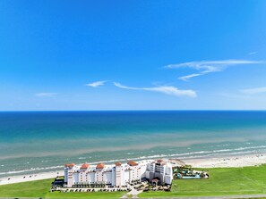 A hotel with multiple white buildings and red roofs, located near a beach with a clear blue sky. - XL Terrace, Lazy River, I-O Pools, Game Room, Spa, Beach, Luxury 2-2 Penthouse! (Galveston)