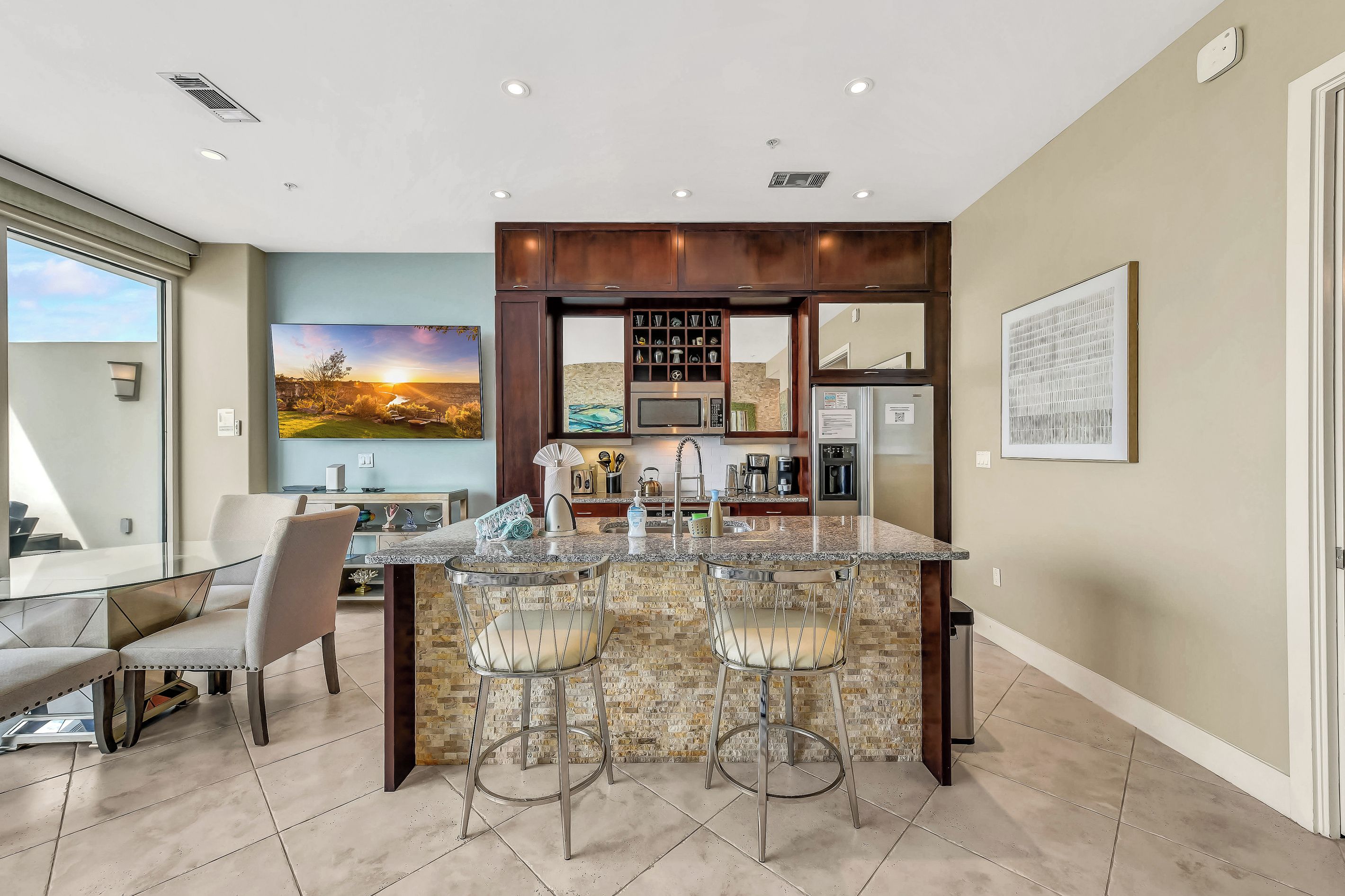 A modern kitchen with a central island, bar stools, and a large window overlooking a scenic view.