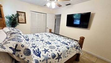A bedroom with a bed, a ceiling fan, a TV, a closet, and a plant.
