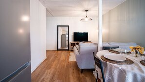 Un salon moderne avec un canapé, une table à manger dressée pour deux personnes, un téléviseur et un plancher en bois.