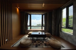 A room with a checkered floor, a central table, two round cushions, and a view through large windows.