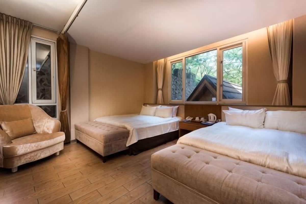 A room with two beds, a sofa, a window with curtains, and a wooden floor.