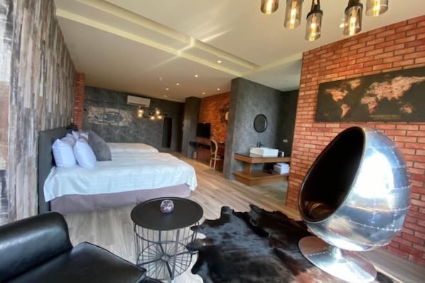 A modern hotel room with a bed, a round table, a leather sofa, and a unique spherical chair.
